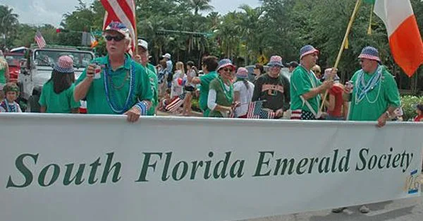 Участники праздничного парада несут плакат South Florida Emerald Society.