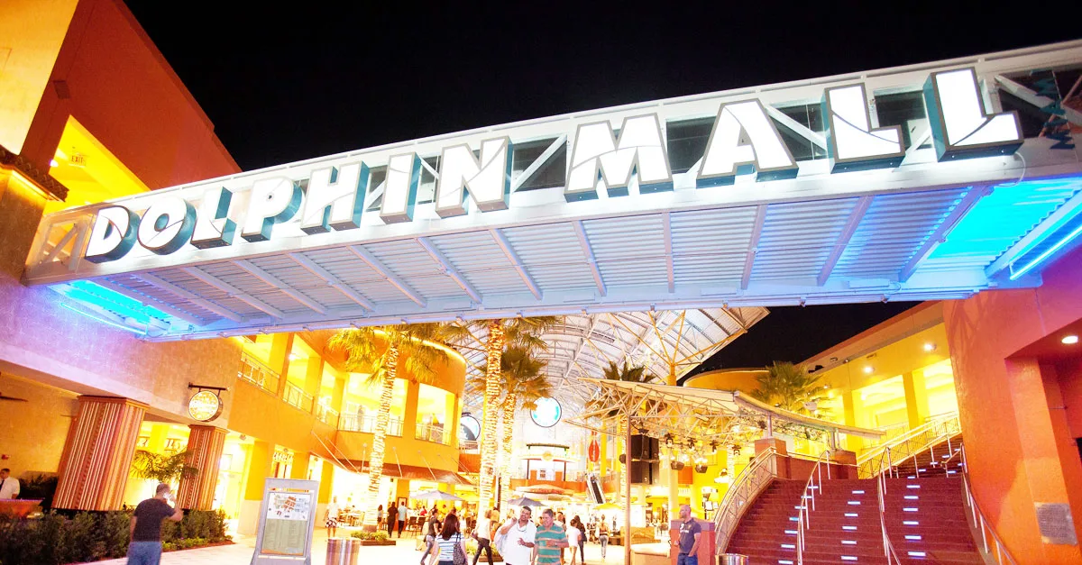 Вход в торговый центр Dolphin Mall с яркой вывеской в ночное время.