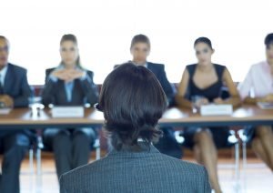 160914-interview-stock-300x212 Executives sitting at conference table, looking at man in foreground