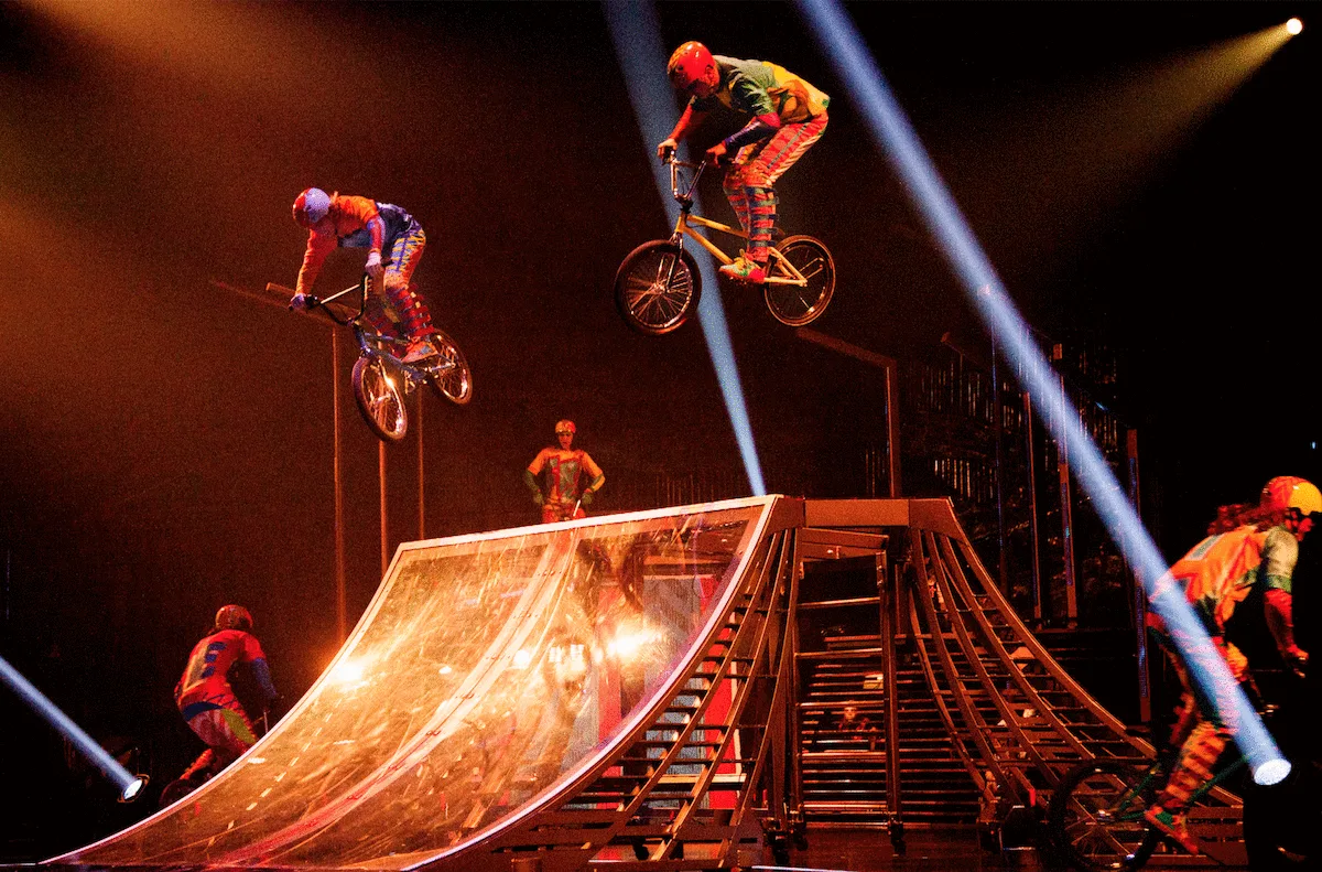Артисты Cirque du Soleil делают трюки на велосипедах BMX под софитами.