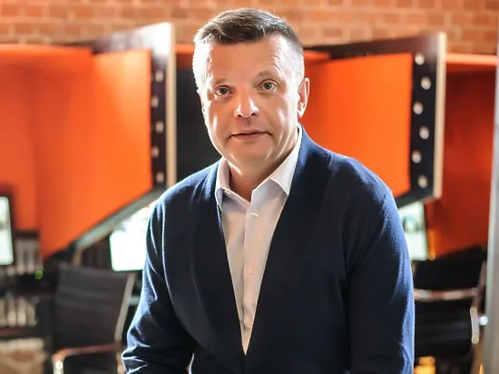 Леонид Парфенов в синем кардигане на фоне современного офиса