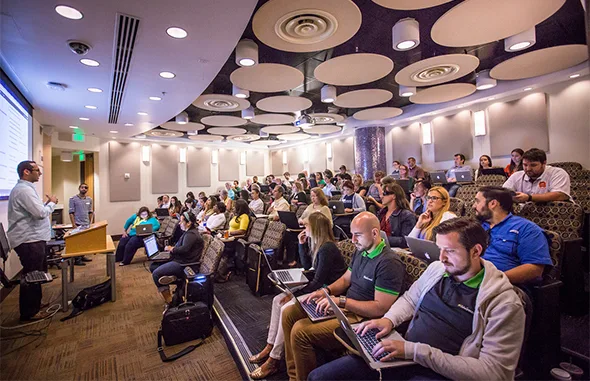 Участники конференции WordCamp с ноутбуками слушают спикера в зале.