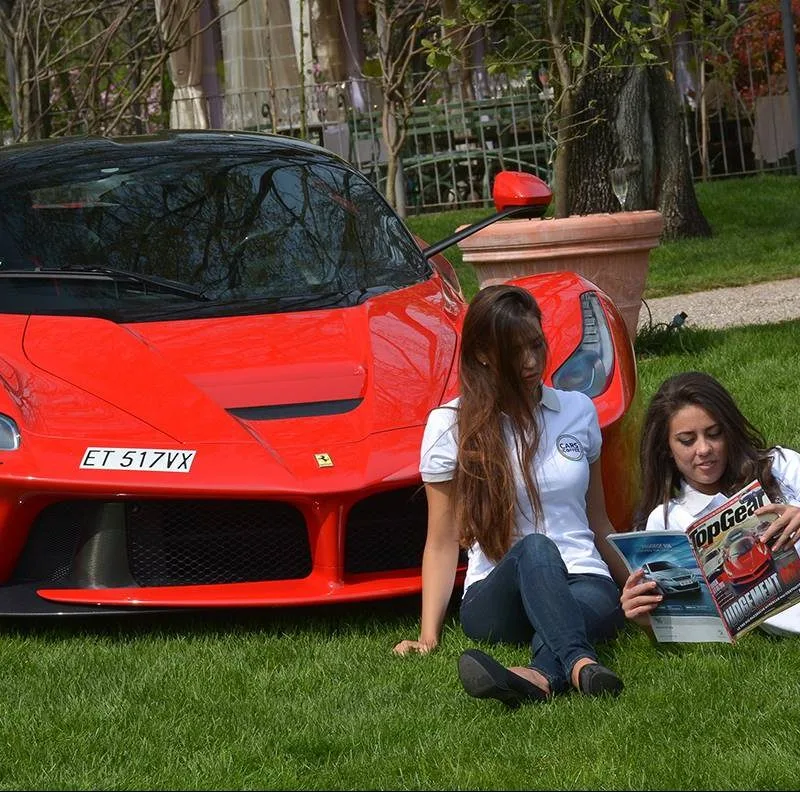 Красный автомобильный спорткар Ferrari и девушки на газоне