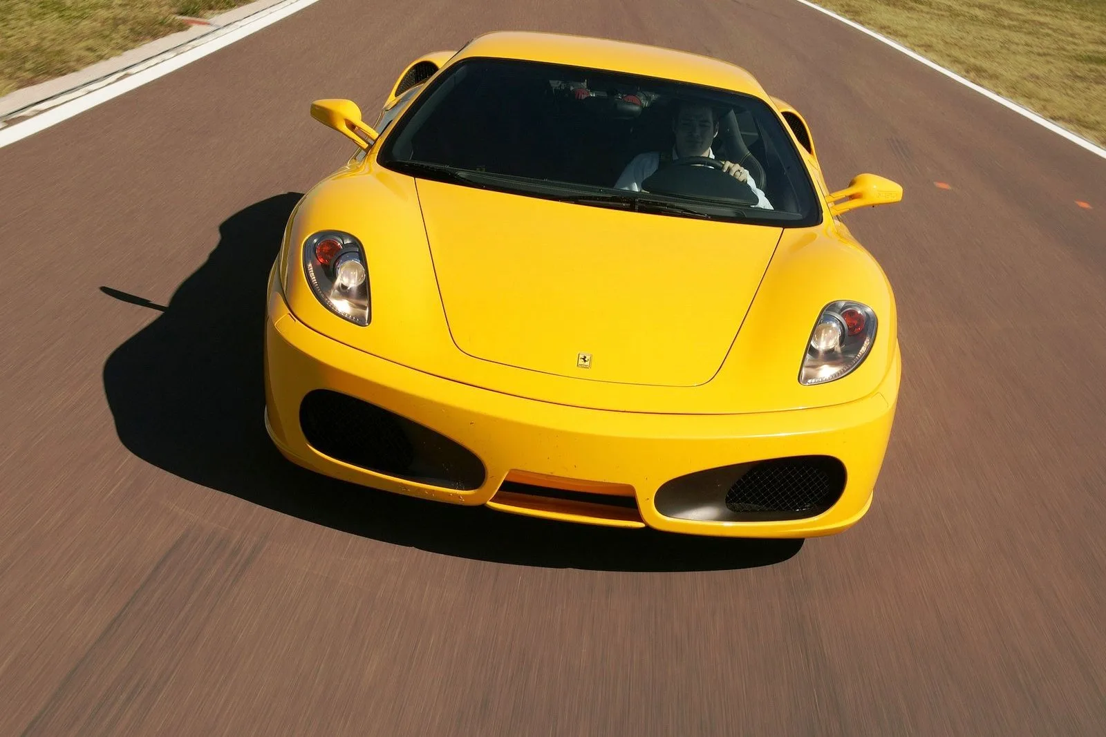 Ярко-желтый автомобиль Ferrari едет по гоночной трассе.