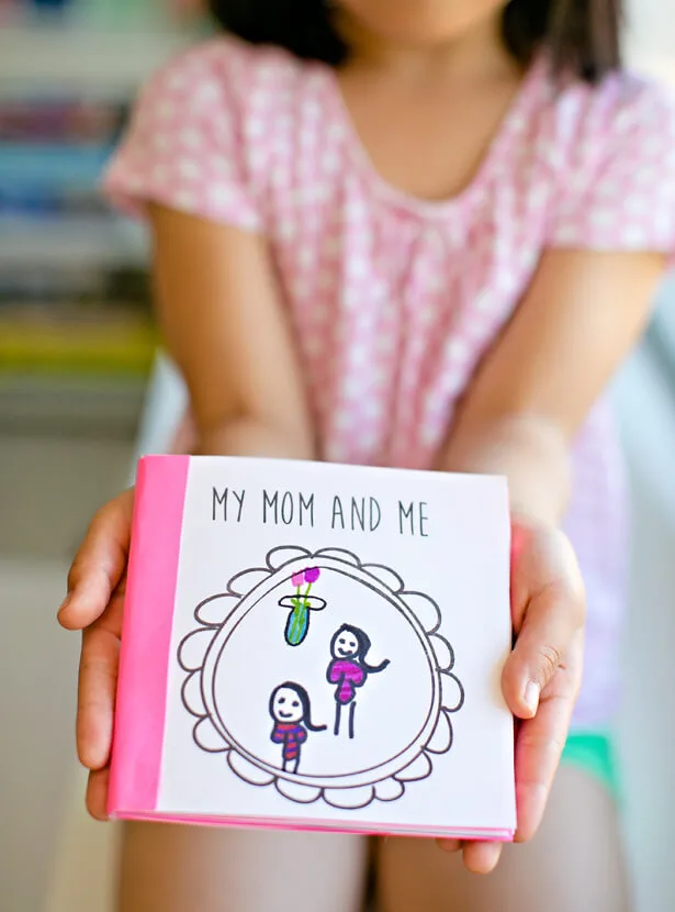 Ребенок держит в руках самодельную открытку с надписью My mom and me