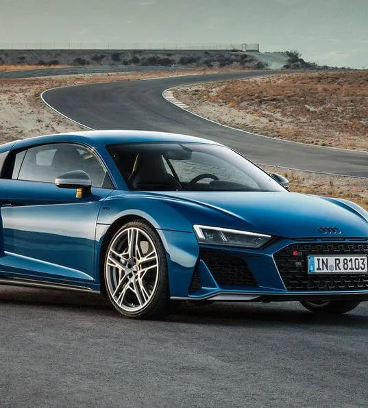 Синий спортивный автомобиль Audi R8 на повороте гоночного трека.