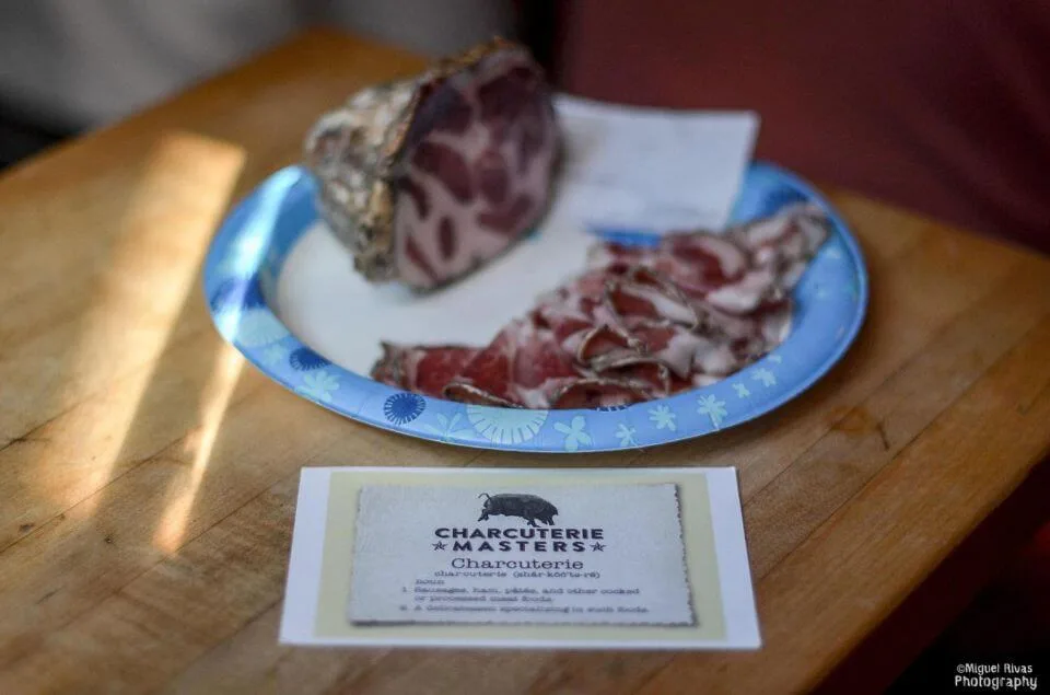 Тарелка с нарезкой мясных деликатесов и карточкой конкурса Charcuterie Masters.