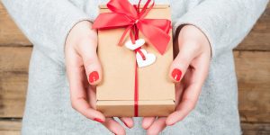 last-minute-valentines-day-gift-today-main-190208_adb8dccc3dad86ecc8589bde86e9edb7-300x150 Hands holding gift in kraft box on a wooden background