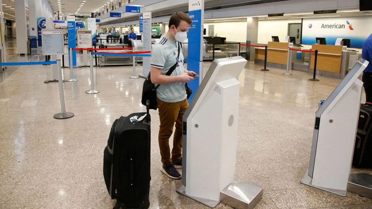 Молодой человек в защитной маске регистрируется у стойки в аэропорту.