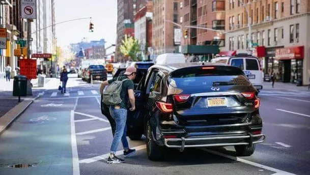 Мужчина с рюкзаком садится в черный автомобиль на улице города